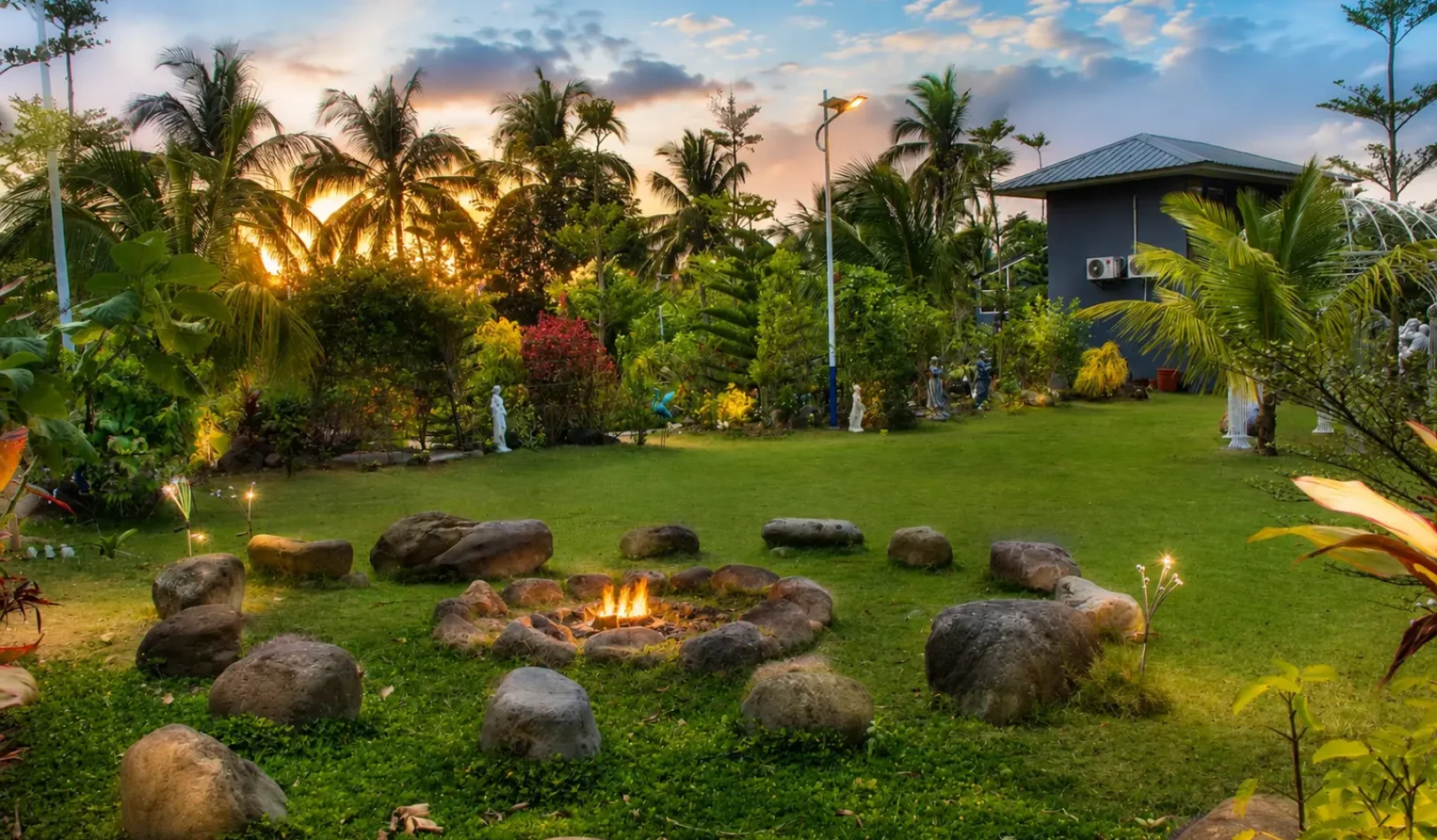 A wide view of the cozy outdoor camp fire area with a stone fire pit lit up under string lights at Wondellea